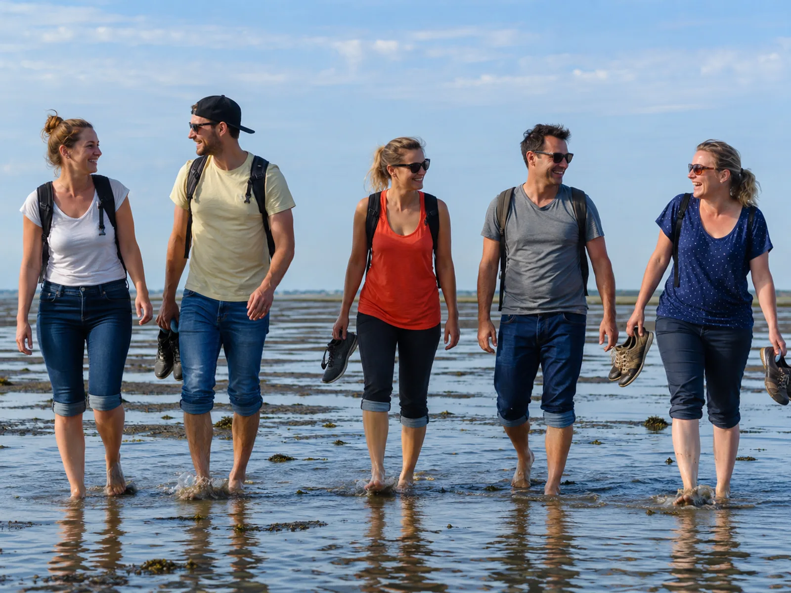 Junge Frauen sitzen lachend im Sand vor einem Strandkorb